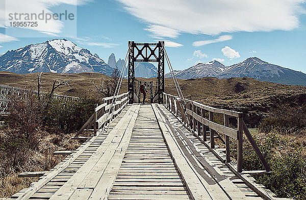 Mann steht auf einer Eisen- und Holzbrücke in der Nähe der Berge Torres del Paine im Hintergrund  Parque Nacional Torres del Paine  Chile