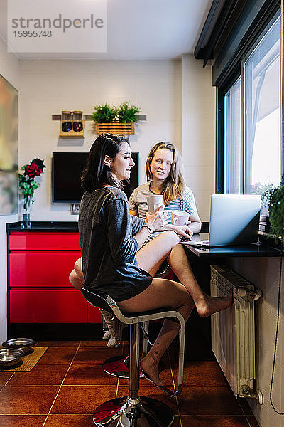 Zwei Frauen sitzen in der Küche und benutzen einen Laptop für einen Videochat