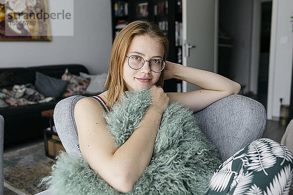 Porträt einer lächelnden jungen Frau  die auf einem Sessel im Wohnzimmer sitzt