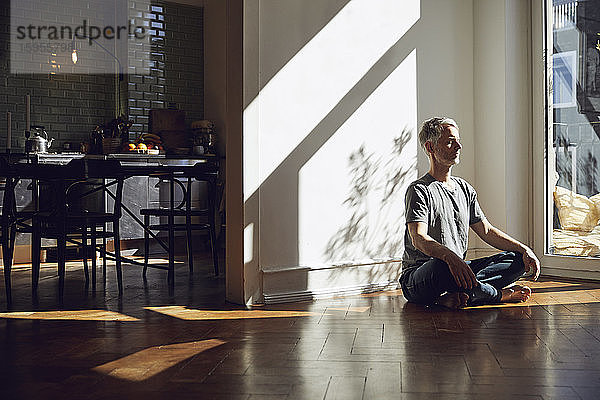Reifer Mann sitzt zu Hause auf dem Boden und meditiert