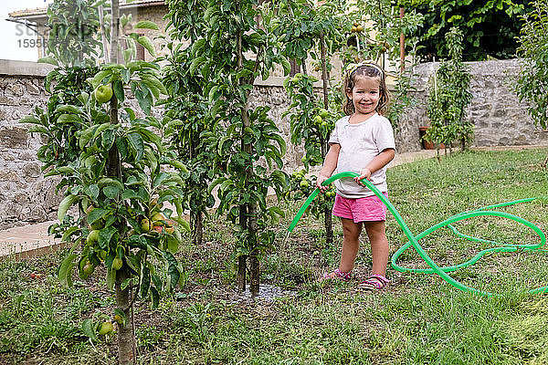Lächelndes kleines Mädchen gießt Baum im Garten
