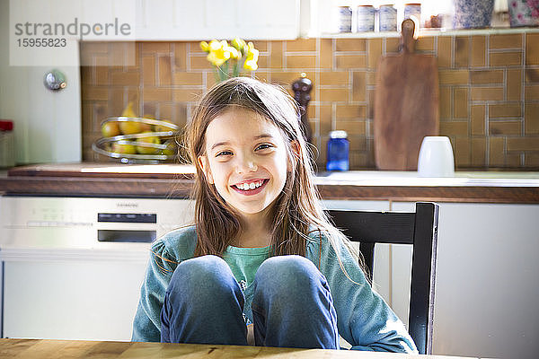 Lächelndes Mädchen sitzt am Küchentisch und schaut in die Kamera