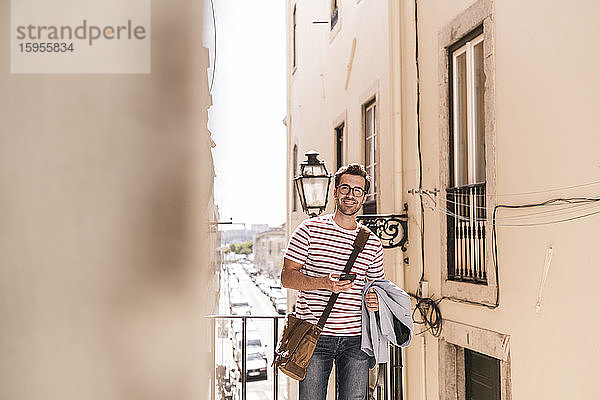Lächelnder junger Mann mit Smartphone in der Stadt  Lissabon  Portugal