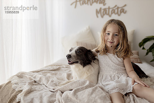 Porträt eines kleinen Mädchens  das mit seinem Hund auf dem Bett sitzt