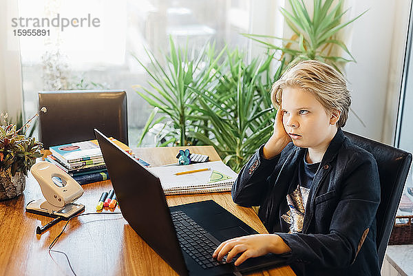 Frustrierter Junge sitzt mit Laptop am Schreibtisch