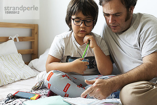 Vater hilft dem Sohn bei den Hausaufgaben  während er zu Hause im Bett sitzt