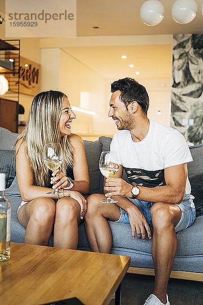 Lachendes Paar auf der Couch sitzend mit Gläsern Weißwein