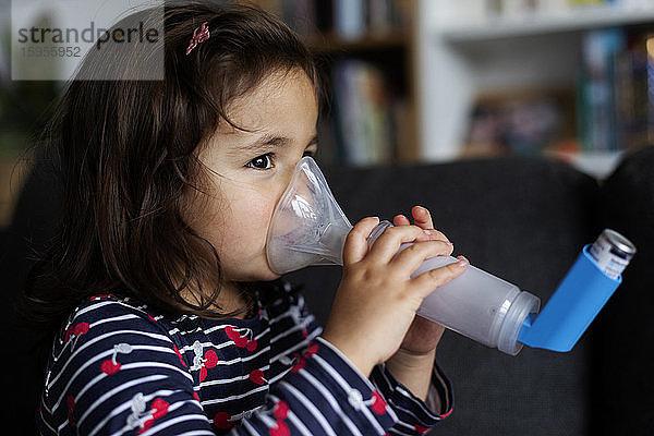 Nahaufnahme eines asthmatischen Mädchens  das zu Hause im Wohnzimmer einen Inhalator benutzt