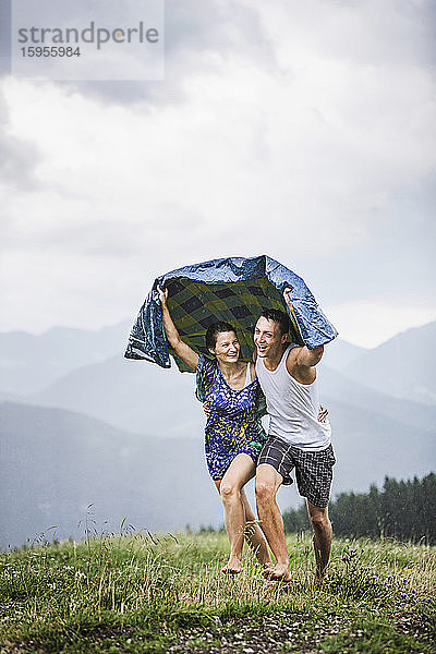 Glückliches Paar läuft bei Regen auf einer Bergwiese  Achenkirch  Österreich