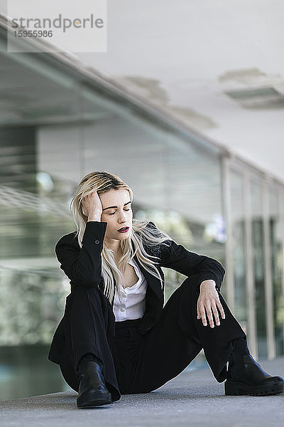 Porträt einer jungen Geschäftsfrau mit geschlossenen Augen vor einem Bürogebäude sitzend