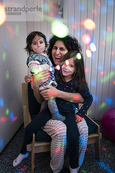 Glückliche Mutter mit zwei Töchtern umgeben von Discolichtern