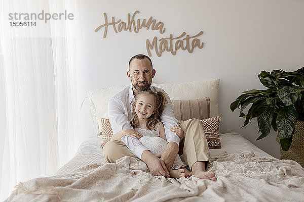 Porträt eines glücklichen Vaters und seiner kleinen Tochter  die zusammen auf dem Bett sitzen