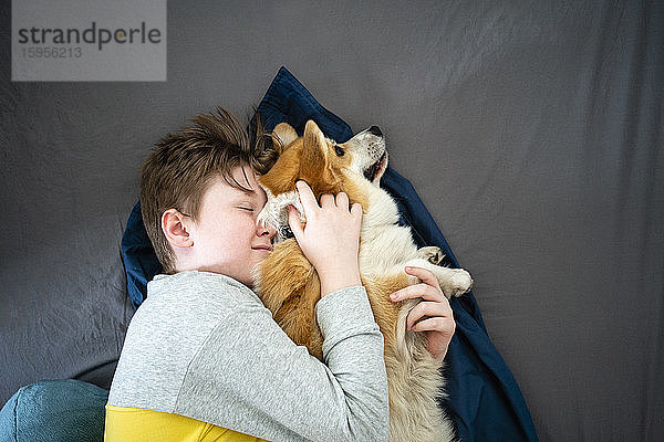 Porträt eines Jungen  der auf dem Bett liegt und seinen Hund kuschelt