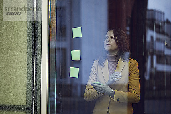 Porträt einer Geschäftsfrau im gelben Anzug hinter einer Fensterscheibe stehend