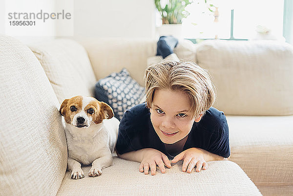 Porträt eines Jungen mit Hund auf dem Sofa liegend im heimischen Wohnzimmer