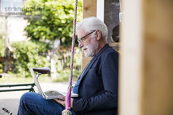Älterer Mann sitzt im Freien und schaut auf den Laptop