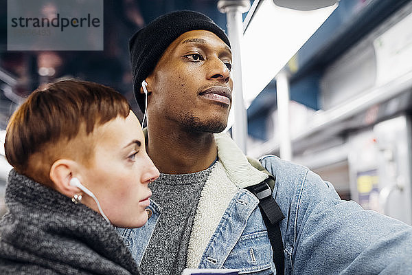 Porträt eines jungen Paares  das sich in einer U-Bahn Ohrstöpsel teilt
