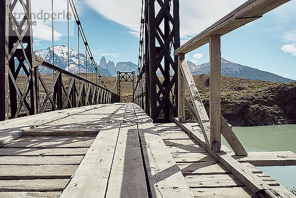 Eisen- und Holzbrücke über das Wasser und die Torres del Paine Berge im Hintergrund  Parque Nacional Torres del Paine  Chile