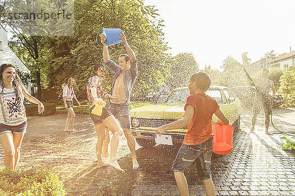 Eine Gruppe von Freunden wäscht im Sommer einen gelben Oldtimer und amüsiert sich