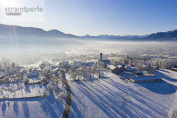 Deutschland  Bayern  Gaissach  Drohnenblick auf schneebedecktes Dorf bei nebligem Sonnenaufgang
