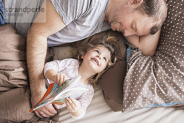 Vater und Tochter lesen ein Buch im Bett