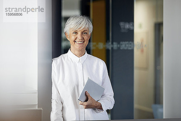 Porträt einer lächelnden älteren Geschäftsfrau mit digitalem Tablett in einem Büro