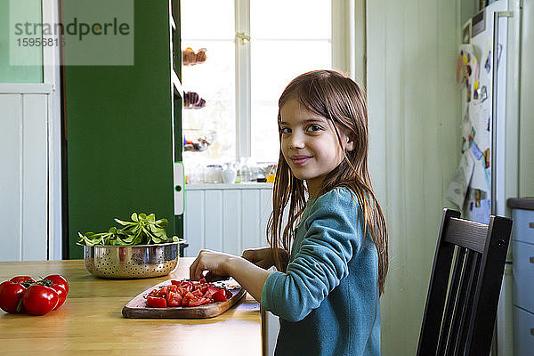 Lächelndes Mädchen schneidet Tomaten auf dem Schneidebrett in der Küche