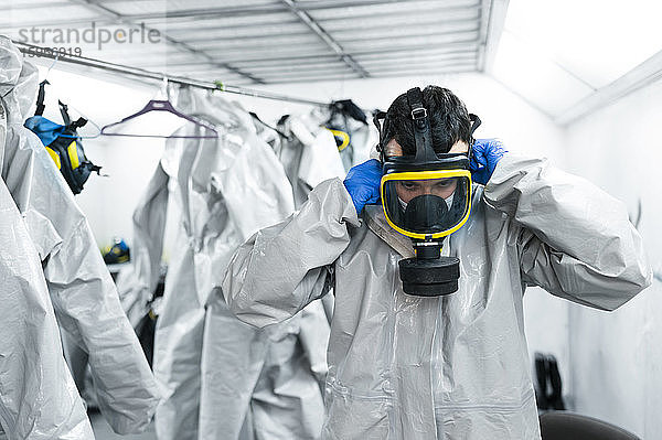 Sanitärarbeiter mit Gasmaske  während er in der Umkleidekabine an einem Schutzanzug steht