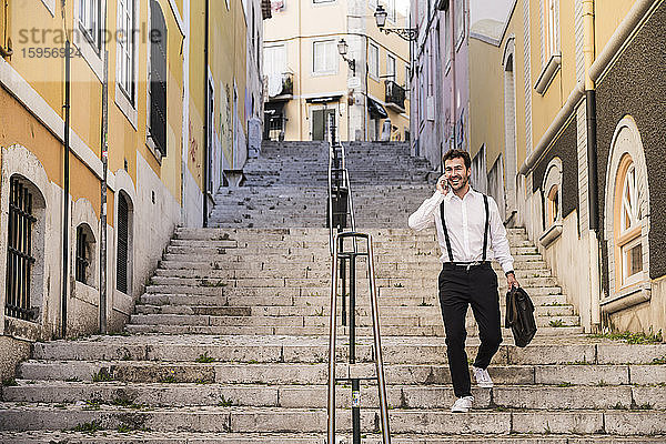 Lächelnder junger Mann am Telefon auf der Treppe in der Altstadt  Lissabon  Portugal