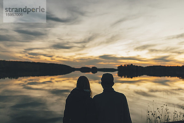 Ehepaar sitzt am See und schaut sich den Sonnenuntergang an