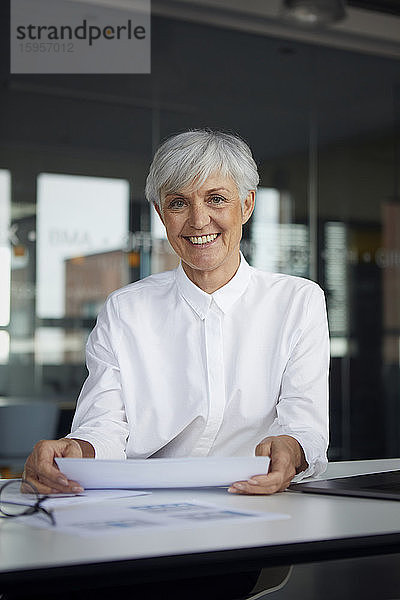 Porträt einer lächelnden älteren Geschäftsfrau am Schreibtisch in ihrem Büro