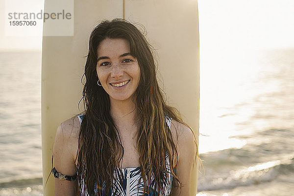 Porträt einer lächelnden jungen Frau mit Surfbrett am Strand  Almeria  Spanien