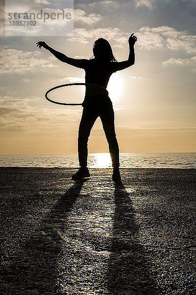 Glückliche Frau spielt mit Hula-Hoop-Reifen im Hafen bei Sonnenuntergang