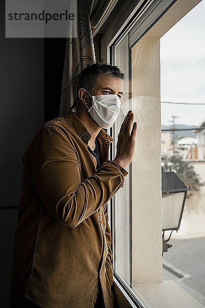 Mann mit Schutzmaske und Blick aus dem Fenster