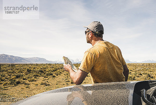 Rückansicht eines Mannes mit Karte am Auto in einer abgelegenen Landschaft in Patagonien  Argentinien