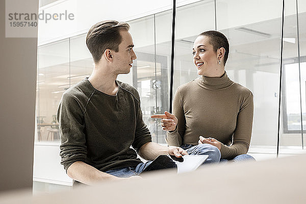 Junge Frau und Mann mit Tablett sprechen am Fenster im Büro