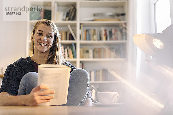 Porträt einer glücklichen jungen Frau  die zu Hause ein Buch liest