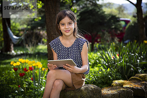 Porträt eines lächelnden Mädchens im Garten sitzend mit digitalem Tablett