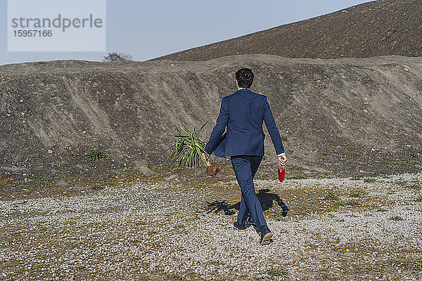 Rückansicht eines Geschäftsmannes mit Pflanze und Kelle  der auf einer stillgelegten Minenhalde läuft