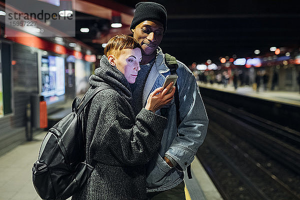 Junges Paar teilt sich ein Smartphone auf dem Bahnsteig