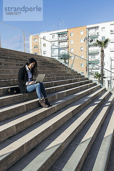 Junge Geschäftsfrau sitzt mit Laptop auf einer Treppe im Freien