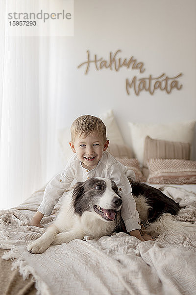 Porträt eines glücklichen kleinen Jungen im Bett mit seinem Hund