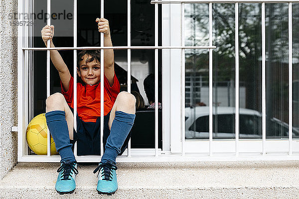 Junge mit Fussball am Fenster  ohne das Haus zum Spielen verlassen zu können