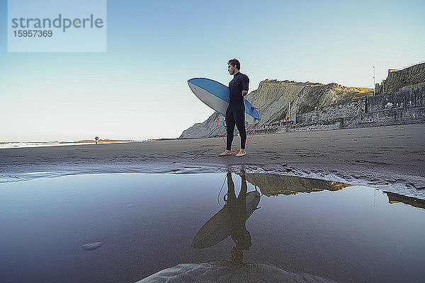 Behinderter Surfer mit Surfbrett am Strand stehend