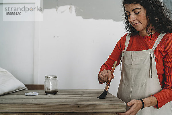 Mittlere erwachsene Frau lackiert Holztisch in ihrem neuen Geschäft