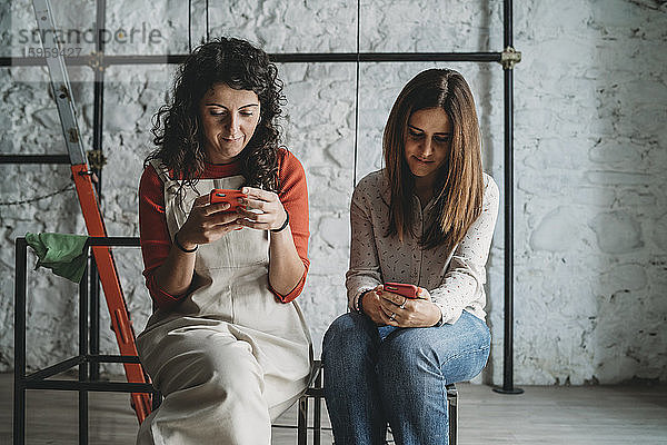 Zwei mittelgroße erwachsene Frauen schauen sich in ihrem neuen Geschäft Smartphones an