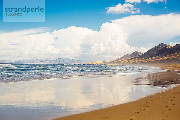 Blick entlang eines Sandstrandes auf Fuerteventura an einem bewölkten Tag.