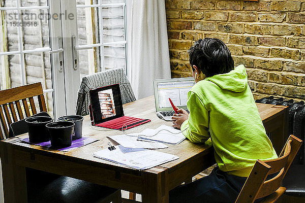 Ein Junge sitzt an einem Schreibtisch und benutzt einen Laptop für eine interaktive Lernsitzung  Hausunterricht  harte Arbeit.