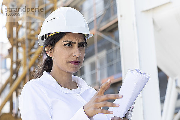 Architektin mit weißem Schutzhelm bei der Arbeit auf der Baustelle.