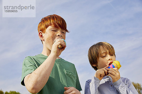 Zwei Jungen stehen im Freien und essen Eistüten.